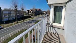 A balcony with a view of a residential street, a clear sky, and a building with a large window. - Bright 3-bedroom Flat by the Beach (Koksijde)