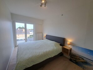 Ein Schlafzimmer mit Bett, Nachttisch, Lampe, Deckenleuchte und Blick durch eine Schiebetür.