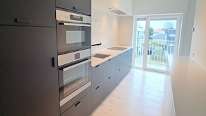 A modern kitchen with dark cabinetry, a built-in oven, and a large window. - Bright 3-bedroom Flat by the Beach (Koksijde)