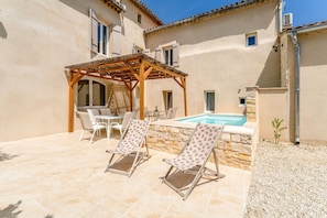 Area piscina con lettini, una pergola e un muro in pietra.