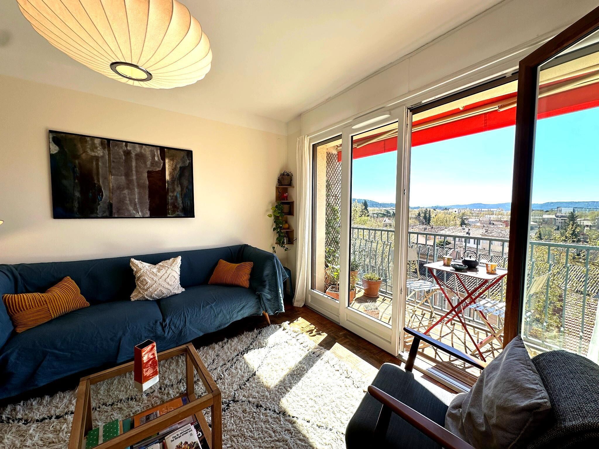 A living room with a sofa, a coffee table, and a view of a balcony with a railing and plants.