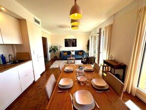 Ein Essbereich mit einem Holztisch, gedeckt für vier Personen, einem blauen Sofa im Hintergrund und einer Küche mit weißen Schränken.