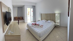 Habitación de hotel con cama, televisor, zona de estar con sofá y un ventanal grande.