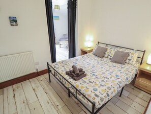A bedroom with a bed, a nightstand, a radiator, and a window with curtains. - Herby's Retreat (Mablethorpe)