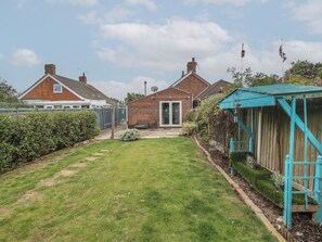 Ein Wohnhausgarten mit Rasenfläche, Holzzaun und einem Haus mit Backsteinfassade.