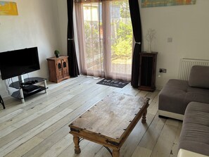 A living room with a wooden coffee table, a television on a stand, a cabinet, a sofa, and a door leading to a balcony with curtains. - Herby's Retreat (Mablethorpe)