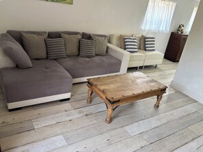 A living room with a grey sectional sofa, a white armchair, a wooden coffee table, and a wooden cabinet. - Herby's Retreat (Mablethorpe)