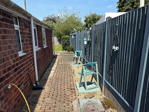 A narrow brick pathway leading to a gated area with a small garden and outdoor seating. - Herby's Retreat (Mablethorpe)