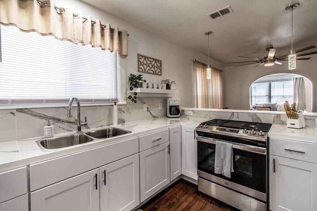 A modern kitchen with white cabinets, a stainless steel stove, and a double sink.