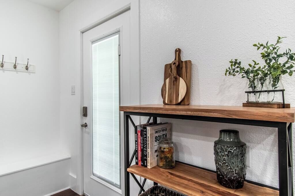 Un couloir avec une porte blanche, une étagère avec des livres et un bocal, et une plante accrochée au mur.