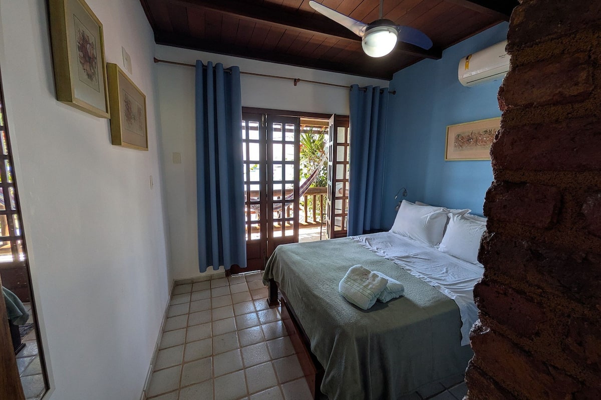 Un dormitorio con cama, ventilador de techo, ventana con cortinas y puerta que da al exterior.