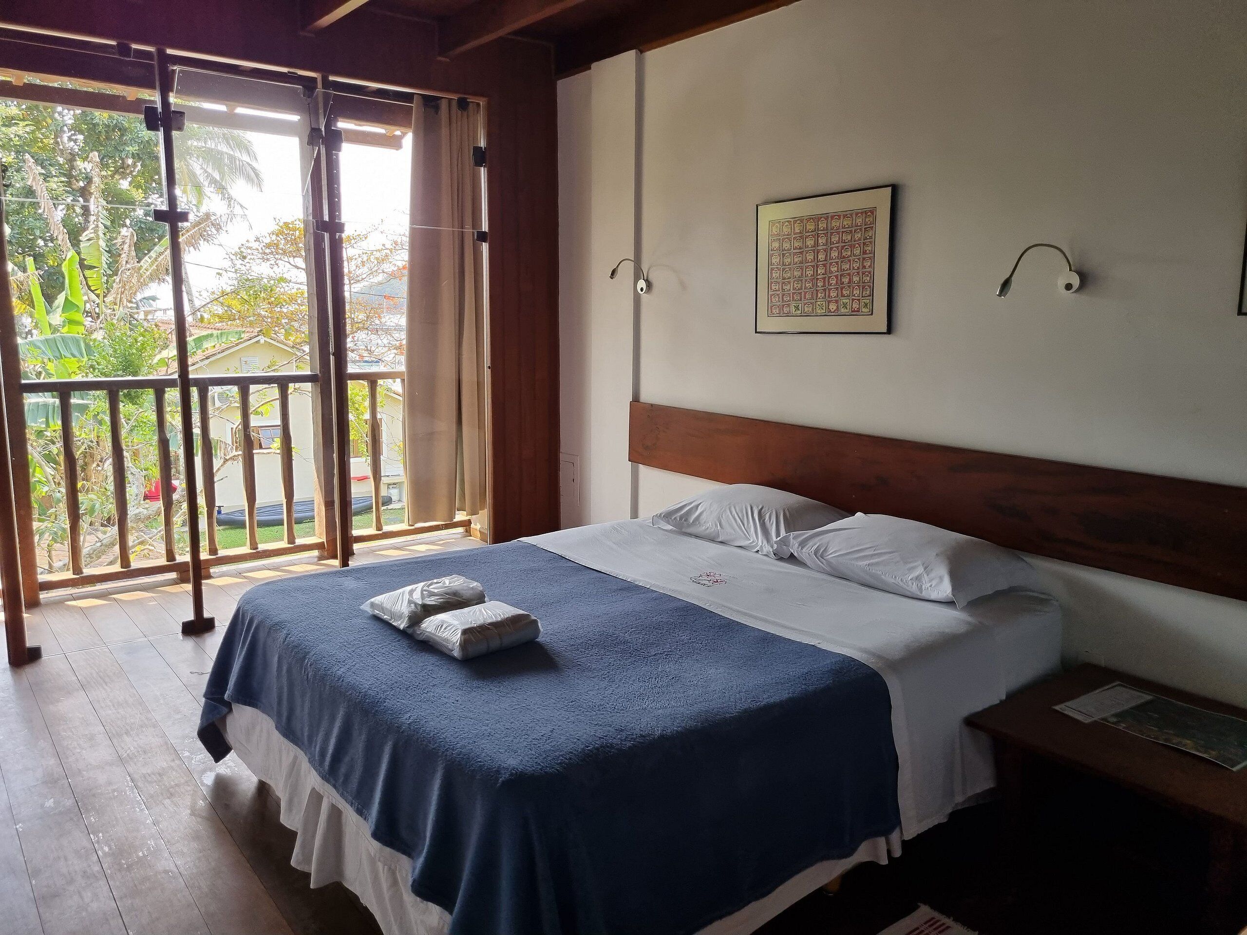 A bedroom with a bed, a wooden headboard, a window with curtains, and a view of greenery outside.