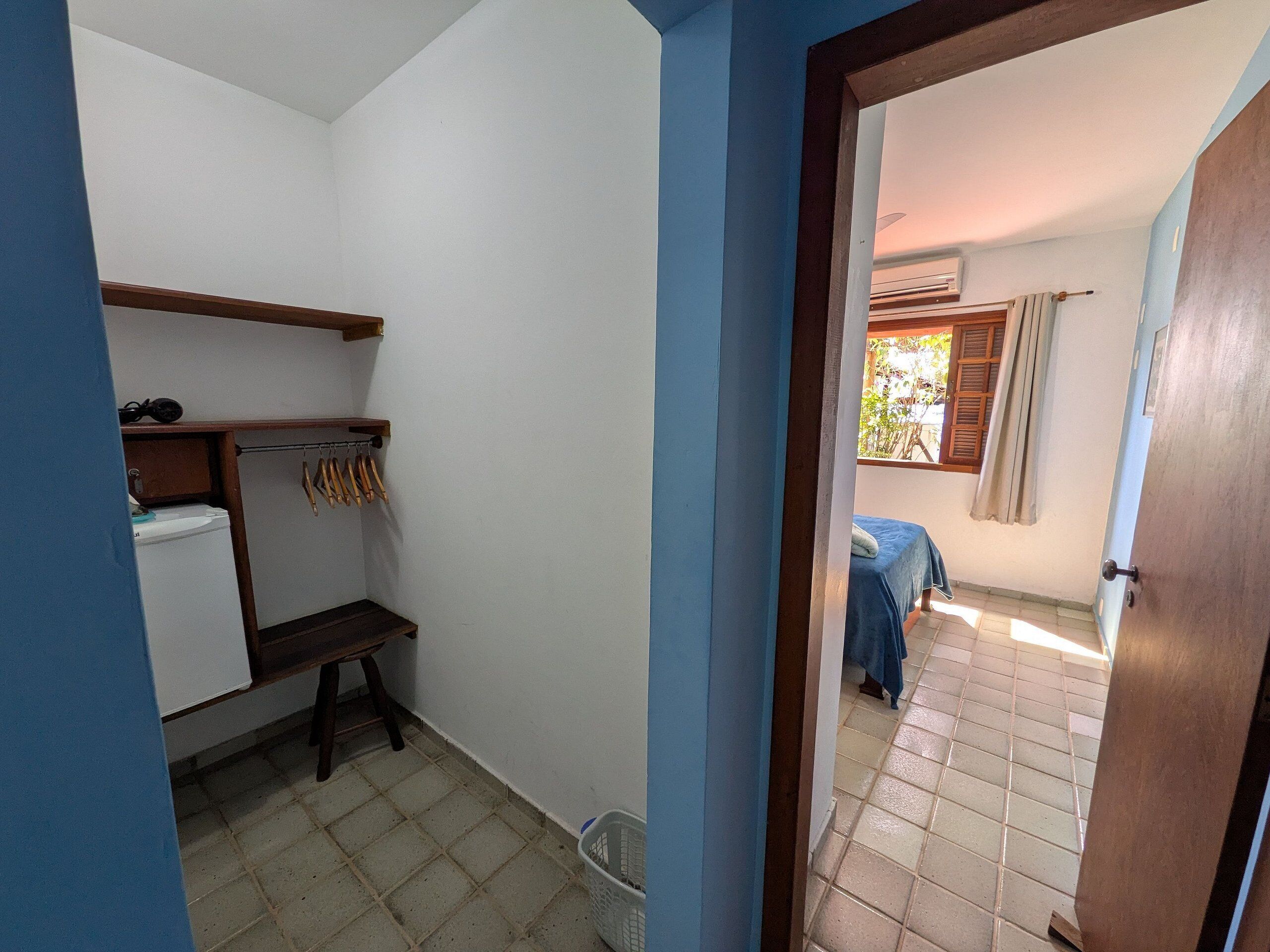 Ein kleines, kompaktes Zimmer mit einem Bett, einer Bank, einem Wäscheständer und einem kleinen Kühlschrank.