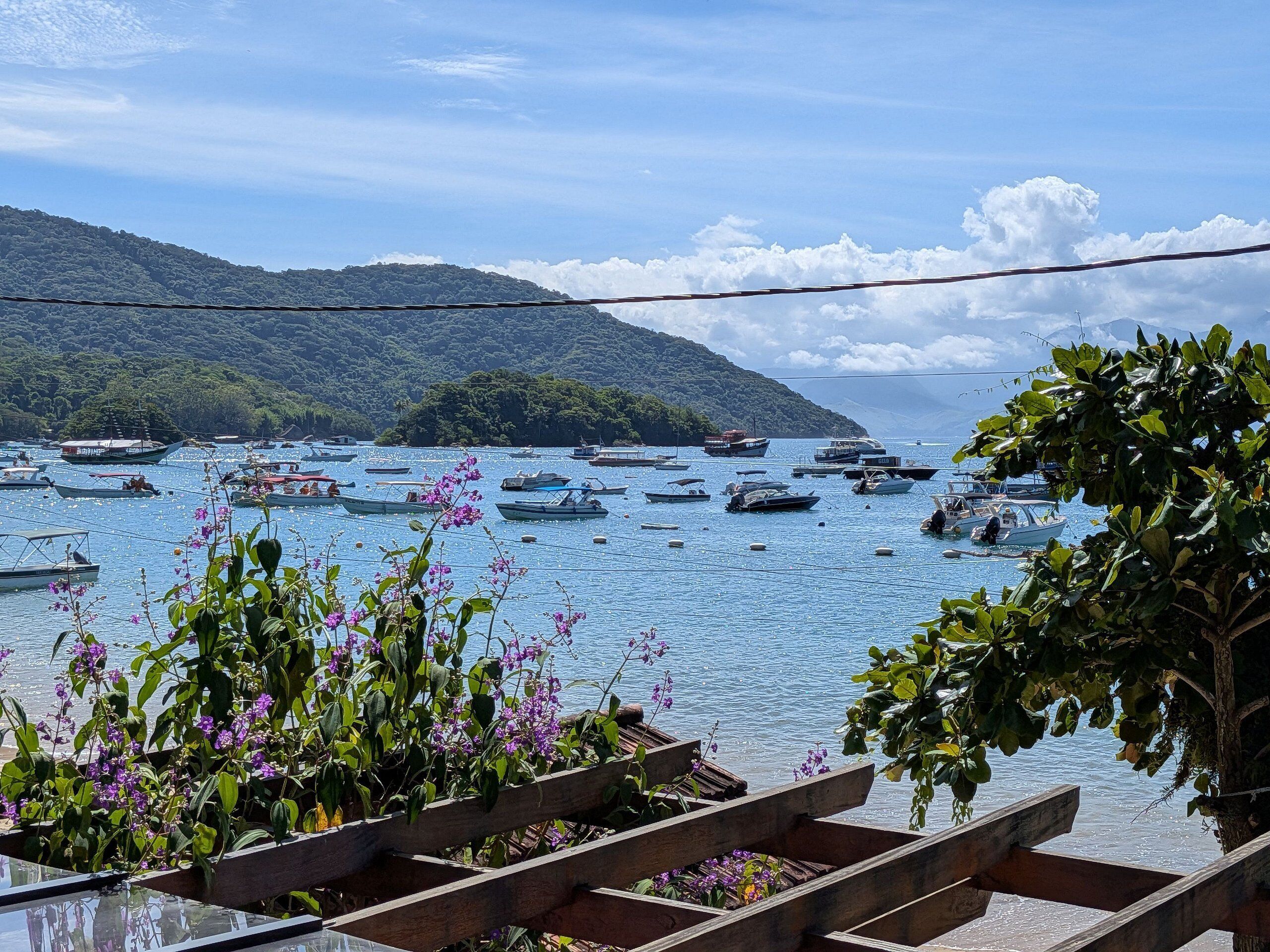 A coastal view with boats, a wooden deck, and a mountain in the background.