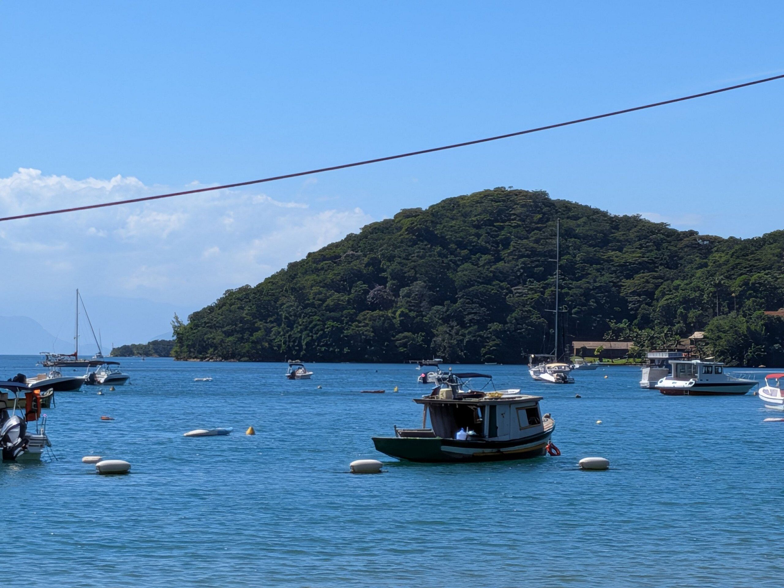 Uma marina costeira com barcos atracados, uma pequena ilha ao fundo e céu claro.