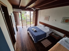 Un dormitorio con cama, mesita de noche, ventilador de techo y ventana con vistas a vegetación.