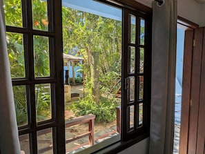 Vista a través de una ventana con marco de madera que muestra un jardín con un banco y un sendero.
