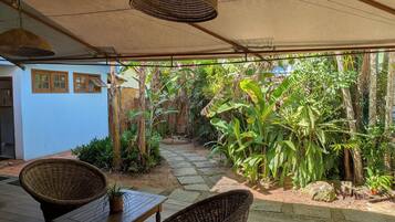 A covered patio with wicker furniture, a stone pathway, and lush tropical plants.