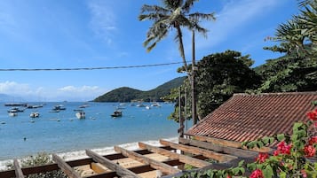 Une vue sur la côte, avec des bateaux, un palmier et une structure en bois surmontée d’un toit en tuiles.