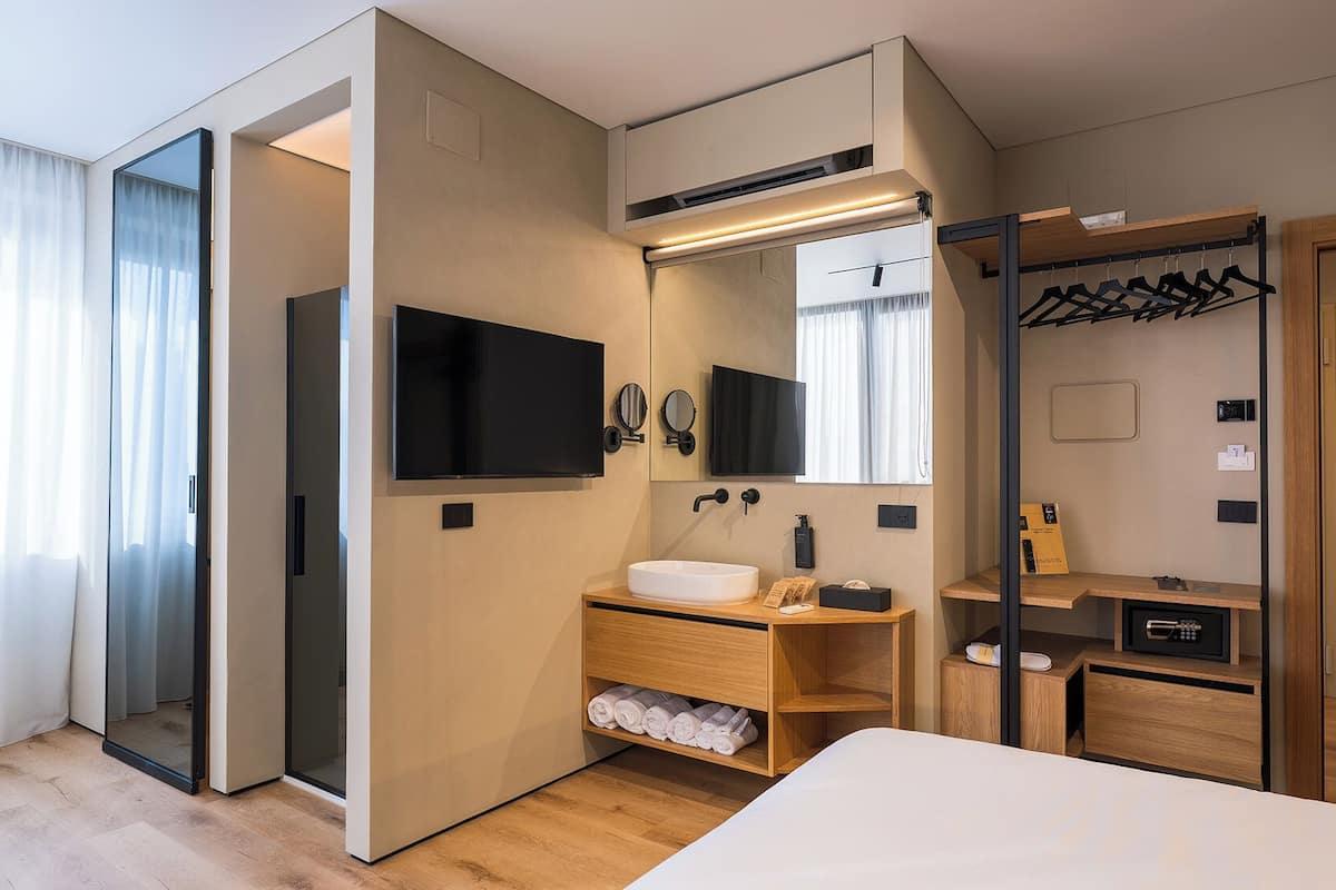 Una habitación de hotel moderna con cama, tocador con lavamanos, televisor, espejo, armario y vestidor.