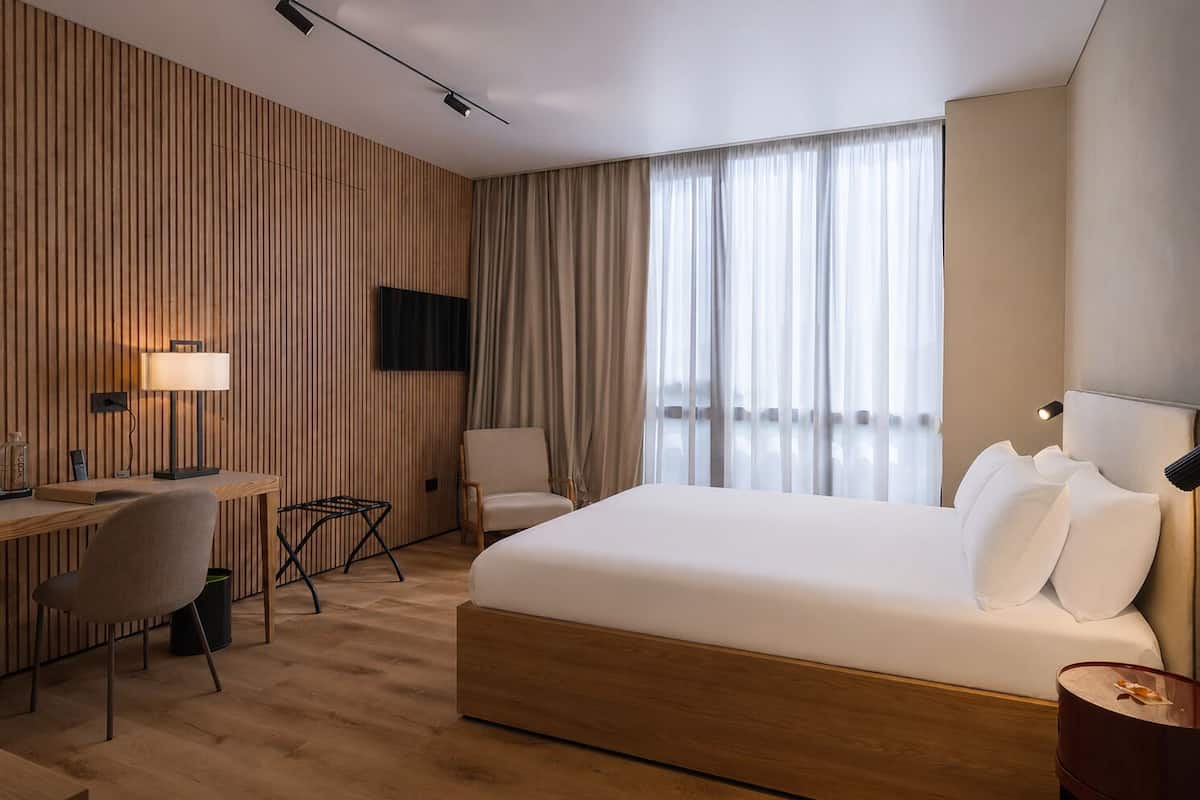 Habitación de hotel con cama, escritorio, silla, televisor y cortinas.