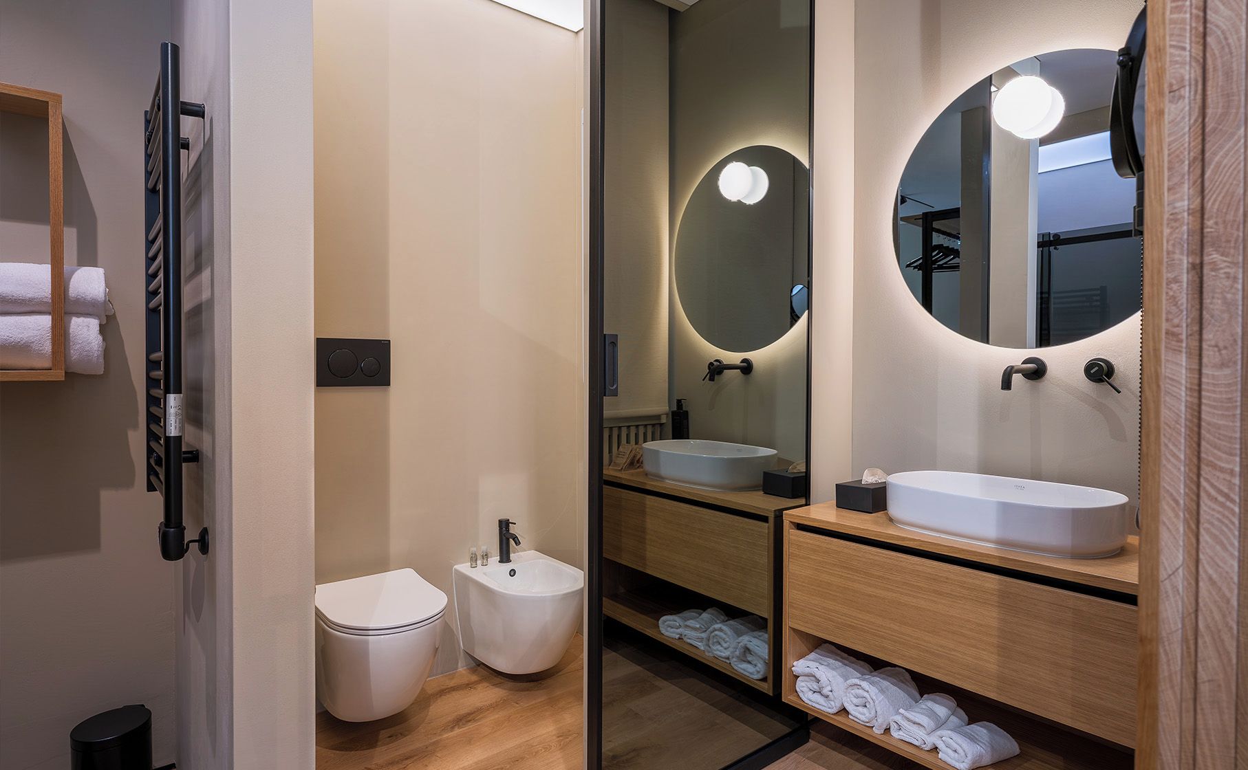 A modern bathroom with a toilet, bidet, and two sinks with mirrors.