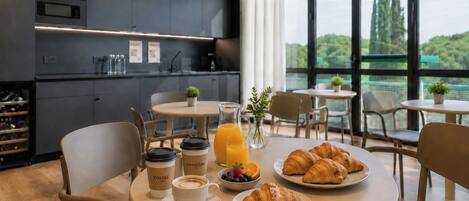 Un desayuno con croissants, café y jugo sobre una mesa, con vista a la vegetación a través de amplias ventanas.