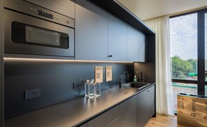 A modern kitchen with a built-in oven, a sink, and a window with a view of greenery. - B&B Campi Diomedei (Foggia)