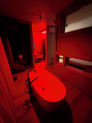 A modern bathroom with a red-lit bathtub, a shower area, and a visible toilet.