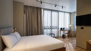 A modern hotel room with a large bed, a desk with a chair, a TV, and a window with curtains.