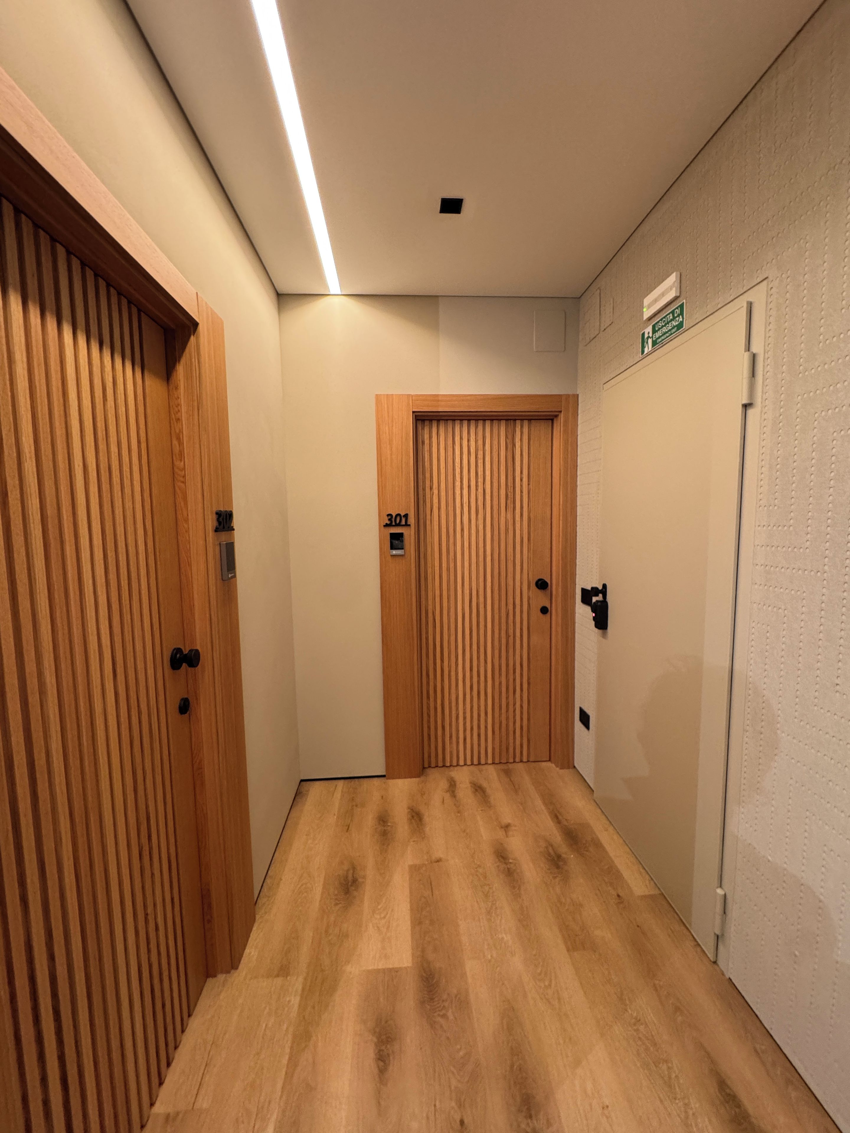 Ein Flur mit Holztüren, einem Schild mit der Zimmernummer 301 und einer strukturierten Wand.