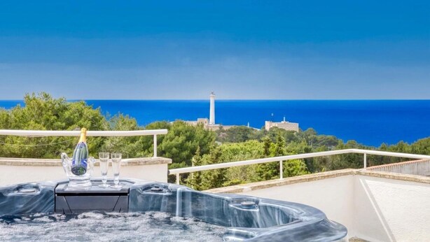 Un jacuzzi con una botella de champán y copas en un balcón con vista al mar y un faro.