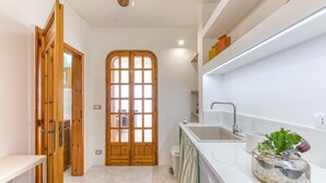 Un pasillo estrecho con una puerta de madera, una cocina con un lavamanos y una encimera con un hervidor.
