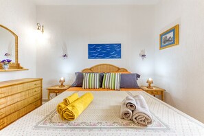Ein Schlafzimmer mit einem Bett, zwei Nachttischen, einer Kommode, einem wandmontierten Spiegel, einem gerahmten Bild und Wandkunst mit Wellenmotiven.