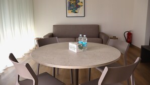A round table with a welcome box and water bottles, surrounded by chairs, in a room with a sofa and a fire extinguisher on the wall. - In a Residence, Air-conditioned, With Terrace (Marone)