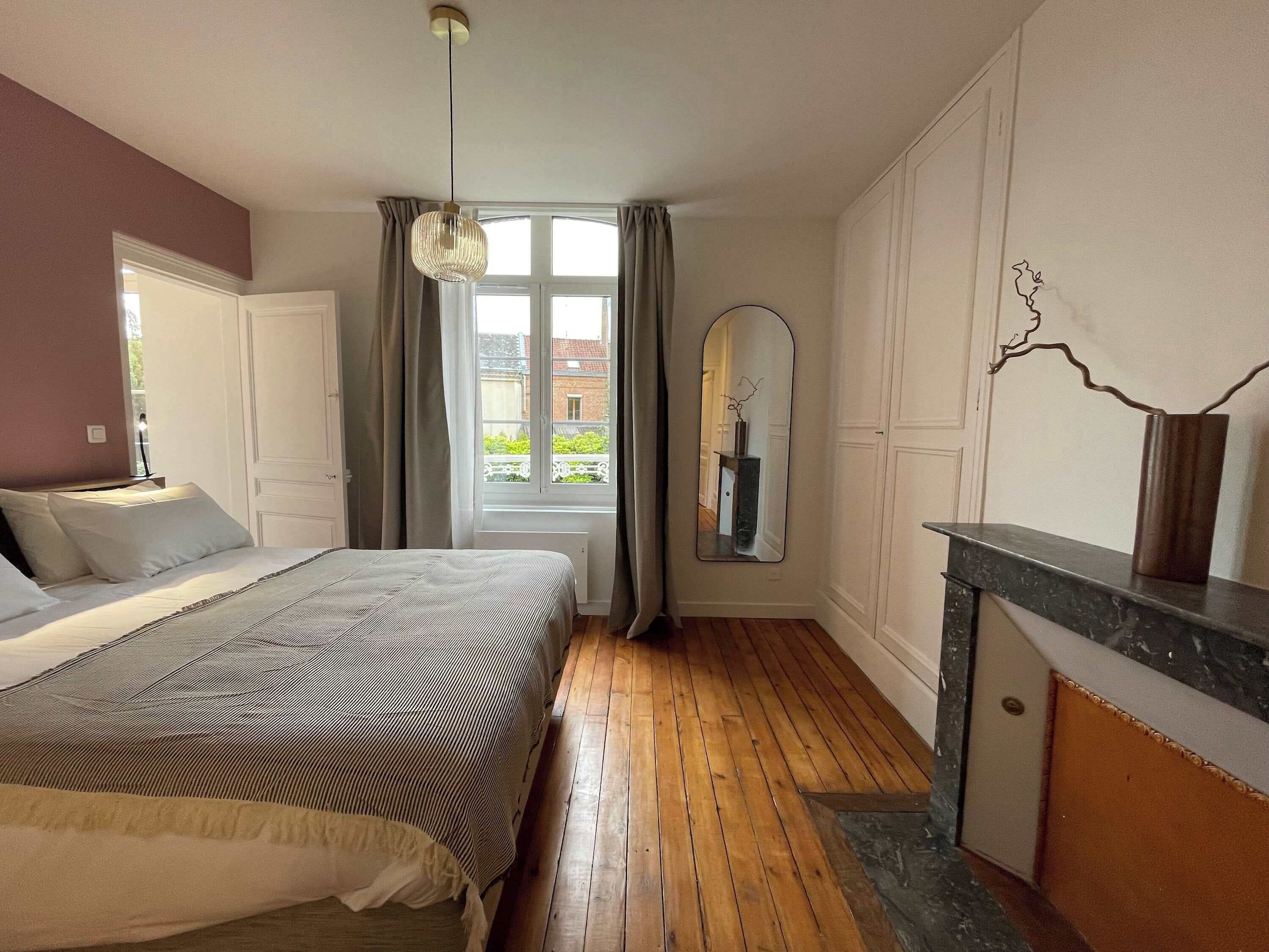 Ein Schlafzimmer mit Bett, einem Fenster mit Vorhängen, einem Spiegel und einem Kamin.