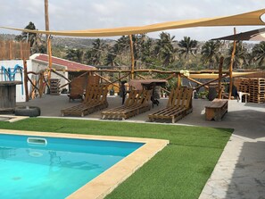 A pool area with wooden loungers, a small table, and a shaded area with a view of palm trees and hills. - Suite with Pool and Nature View (Achada Fazenda)