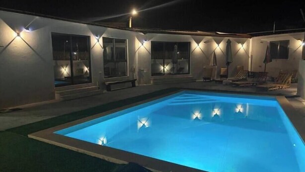 Una piscina illuminata, una zona patio coperta e un edificio con finestre.