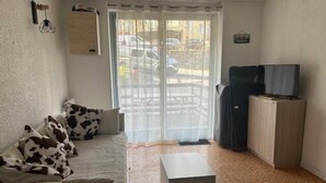 A living room with a sofa, a coffee table, a TV on a cabinet, and a window with curtains. - South-facing terrace studio in resort center (Enchastrayes)