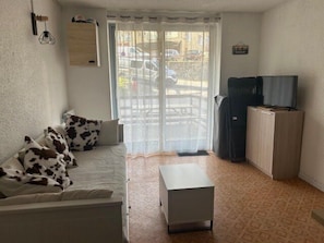 A living room with a sofa, a coffee table, a TV on a cabinet, and a window with curtains. - South-facing terrace studio in resort center (Enchastrayes)