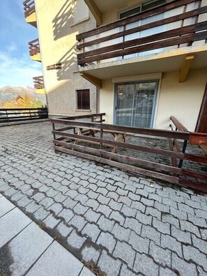 A balcony with wooden railings, a small table, and a window. - South-facing terrace studio in resort center (Enchastrayes)