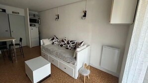 A compact living space with a sofa, a small table, a chair, a radiator, and a kitchenette. - South-facing terrace studio in resort center (Enchastrayes)