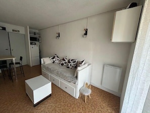 A compact living space with a sofa, a small table, a chair, a radiator, and a kitchenette. - South-facing terrace studio in resort center (Enchastrayes)