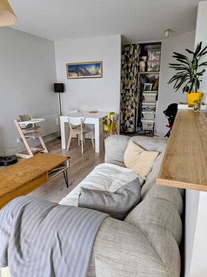 A modern living room with a sofa, a coffee table, a dining table with chairs, a bookshelf, and a plant. - Lyon Center Apartment with private garden & garage (Lyon)