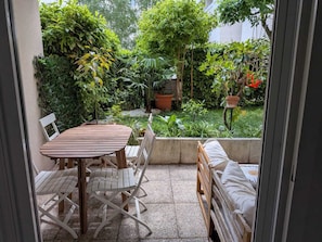 A patio with a wooden table and chairs, a cushioned bench, and a view of a lush garden. - Lyon Center Apartment with private garden & garage (Lyon)
