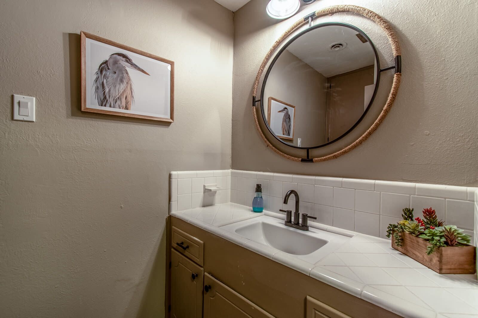 A bathroom with a sink, mirror, framed artwork, and a potted plant.