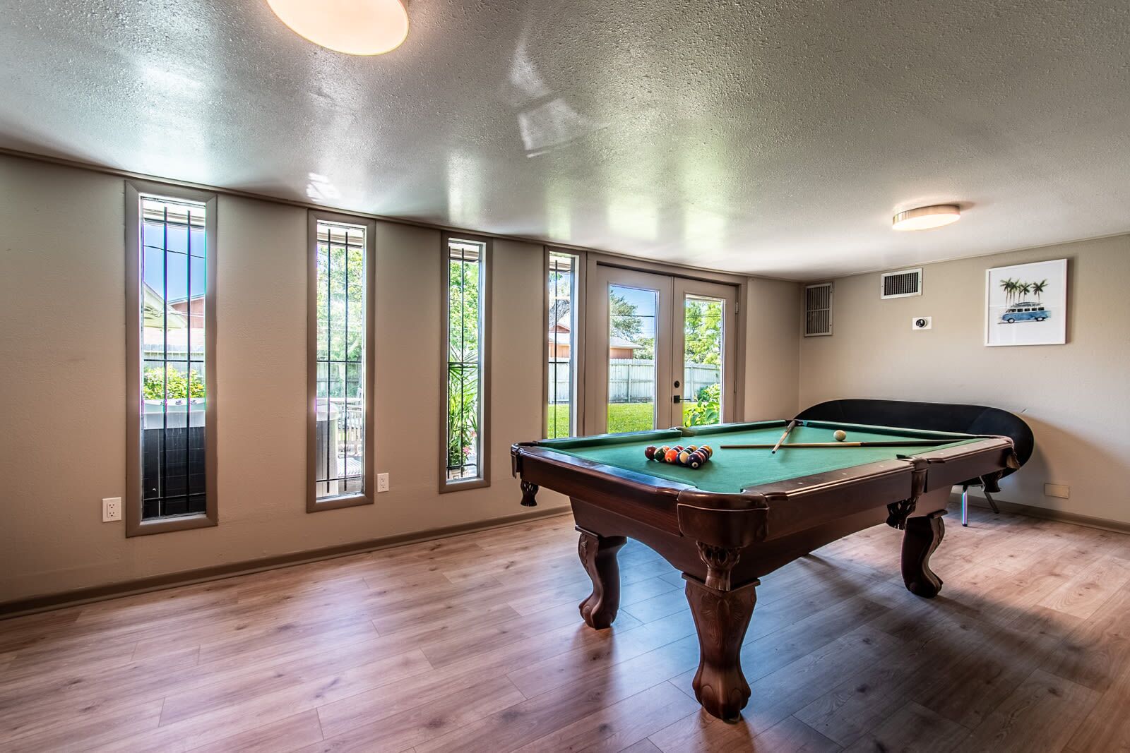 Une table de billard dans une pièce dotée de grandes fenêtres et d’un luminaire au plafond.