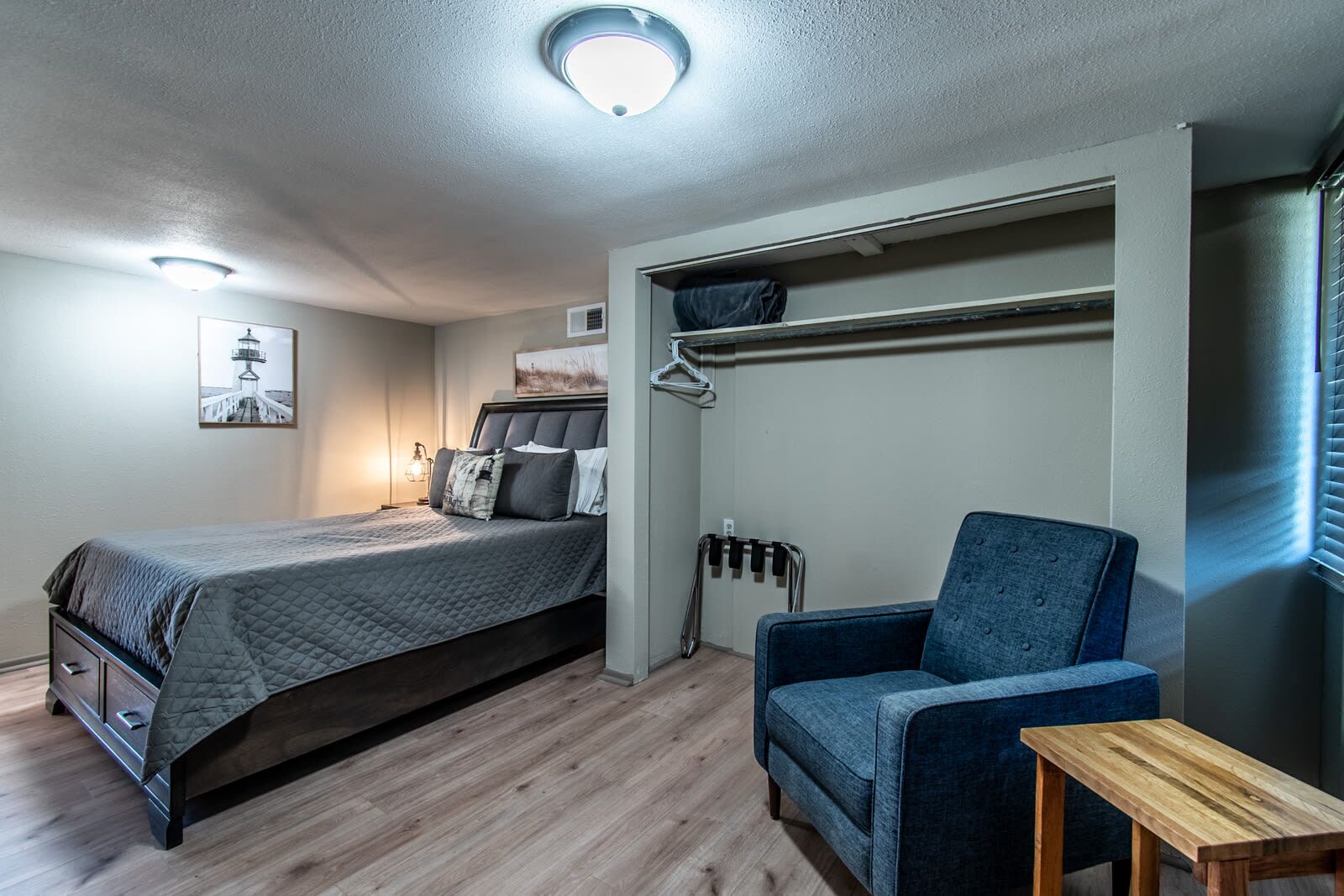 A bedroom with a bed, a chair, a small table, a wardrobe, and a ceiling light.