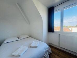 Ein Schlafzimmer mit einem Bett, zwei Kissen, zwei gerollten Handtüchern, einem Fenster mit Blick und einer Heizung.