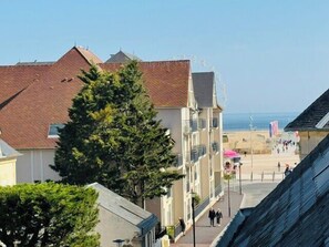 Ein Küstengebäude mit Balkon, einem Baum im Vordergrund und einem Strand im Hintergrund.
